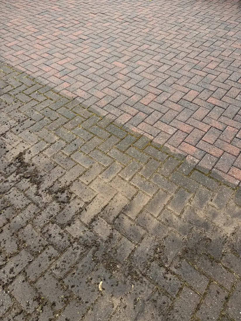 Block-paved driveway part-way through pressure washing, with the cleaned section above and the untreated section below