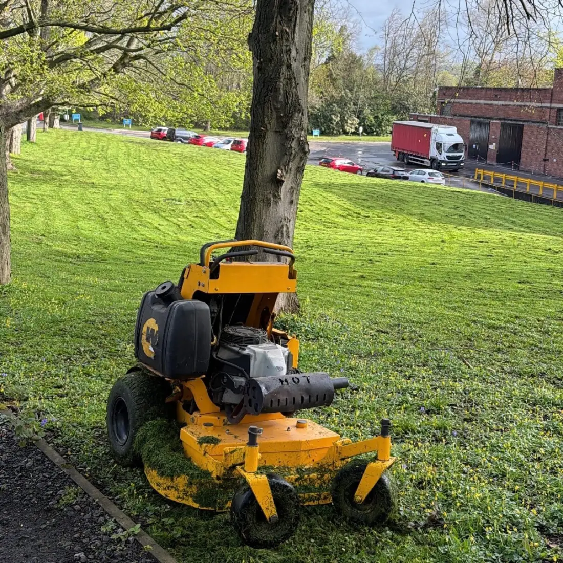 Ride-on mower on site at a commercial premises, with an HGV lorry and industrial building in the background