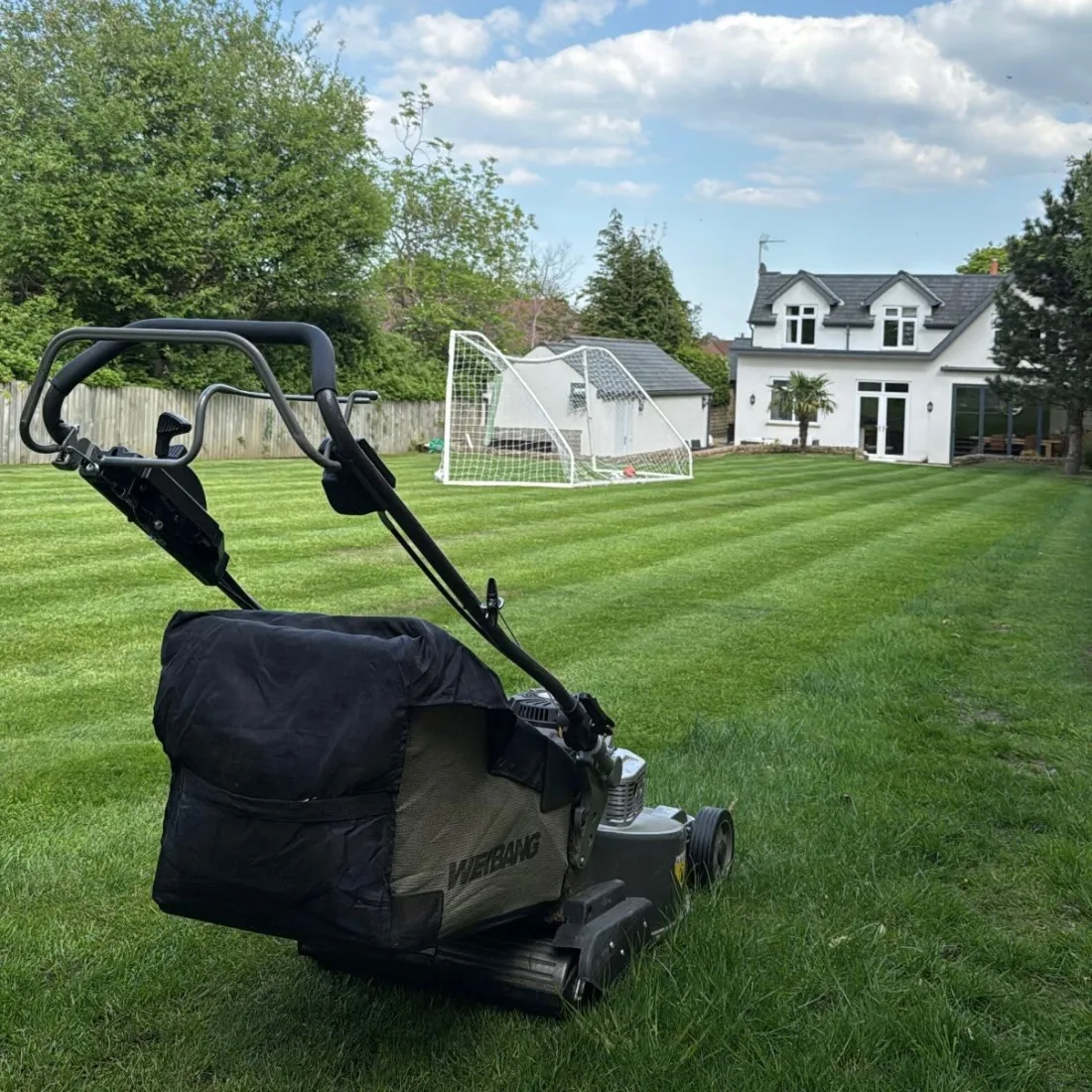 Large striped lawn in a residential garden with a football goal, freshly mown in neat lines up to the house