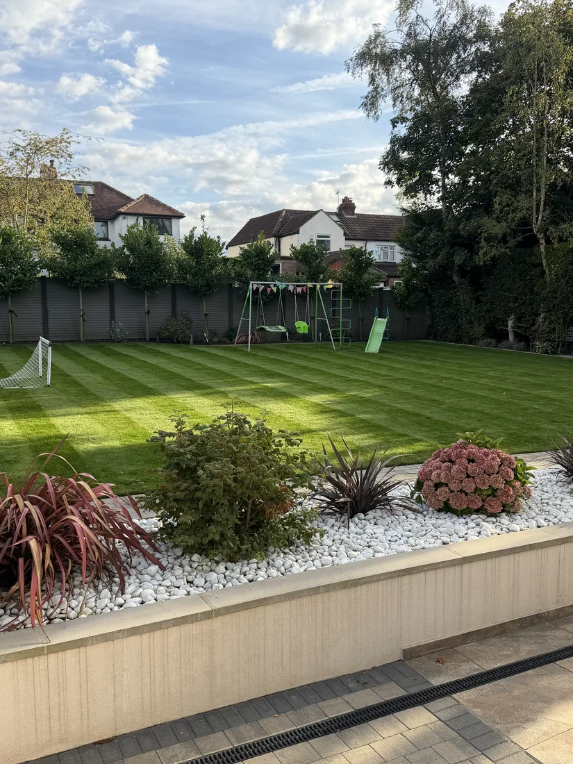 Freshly striped lawn with a raised planting bed and white pebble border in a large residential garden